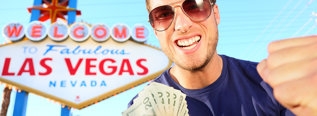 Man Holding Cash in Front of Las Vegas Sign