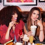 group of girls enjoying milkshake, fries, burgers, and other options at a booth in a restaurant